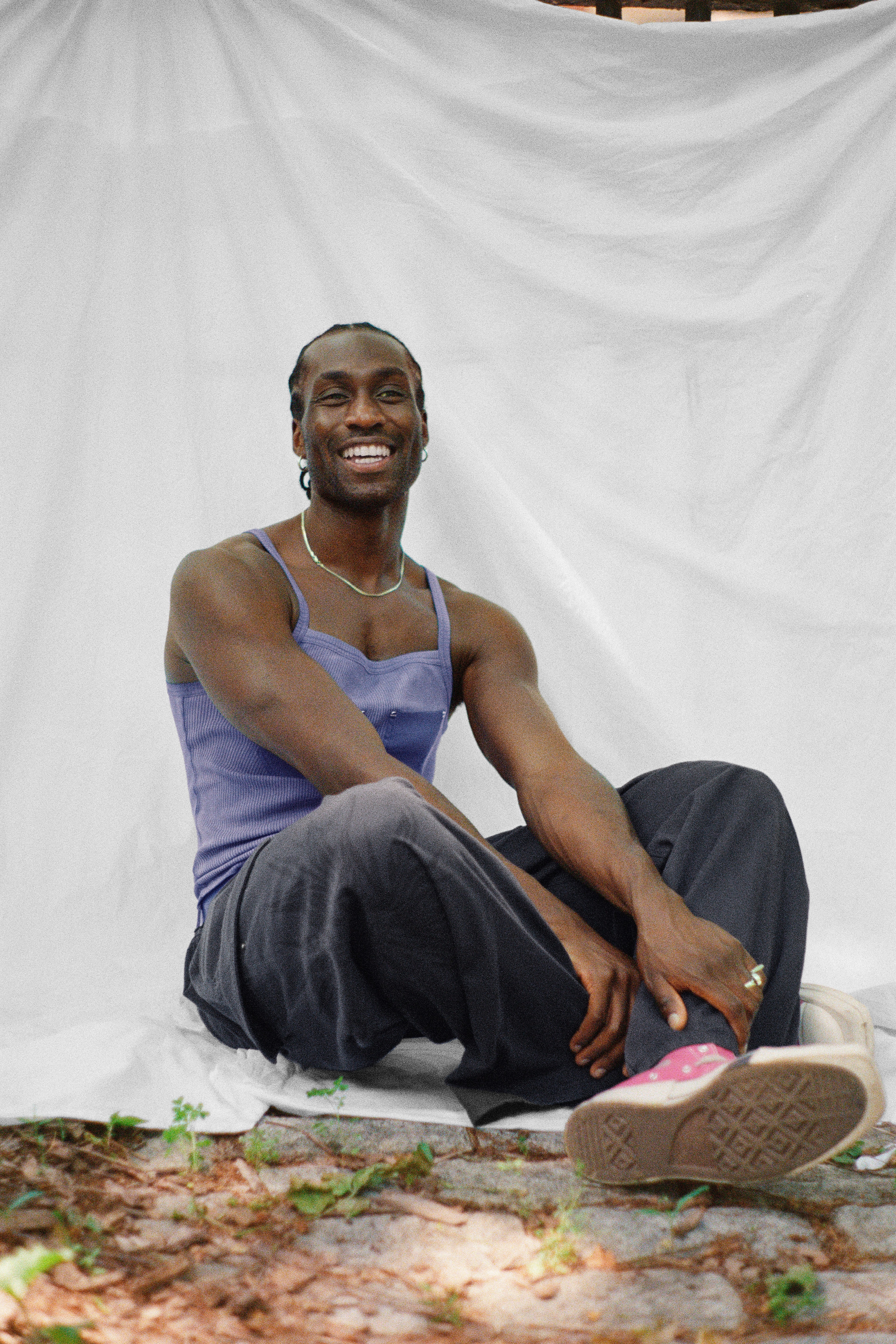 DeVonn sitting down with his legs crossed and smiling looking off to the right with a white fabric back drop