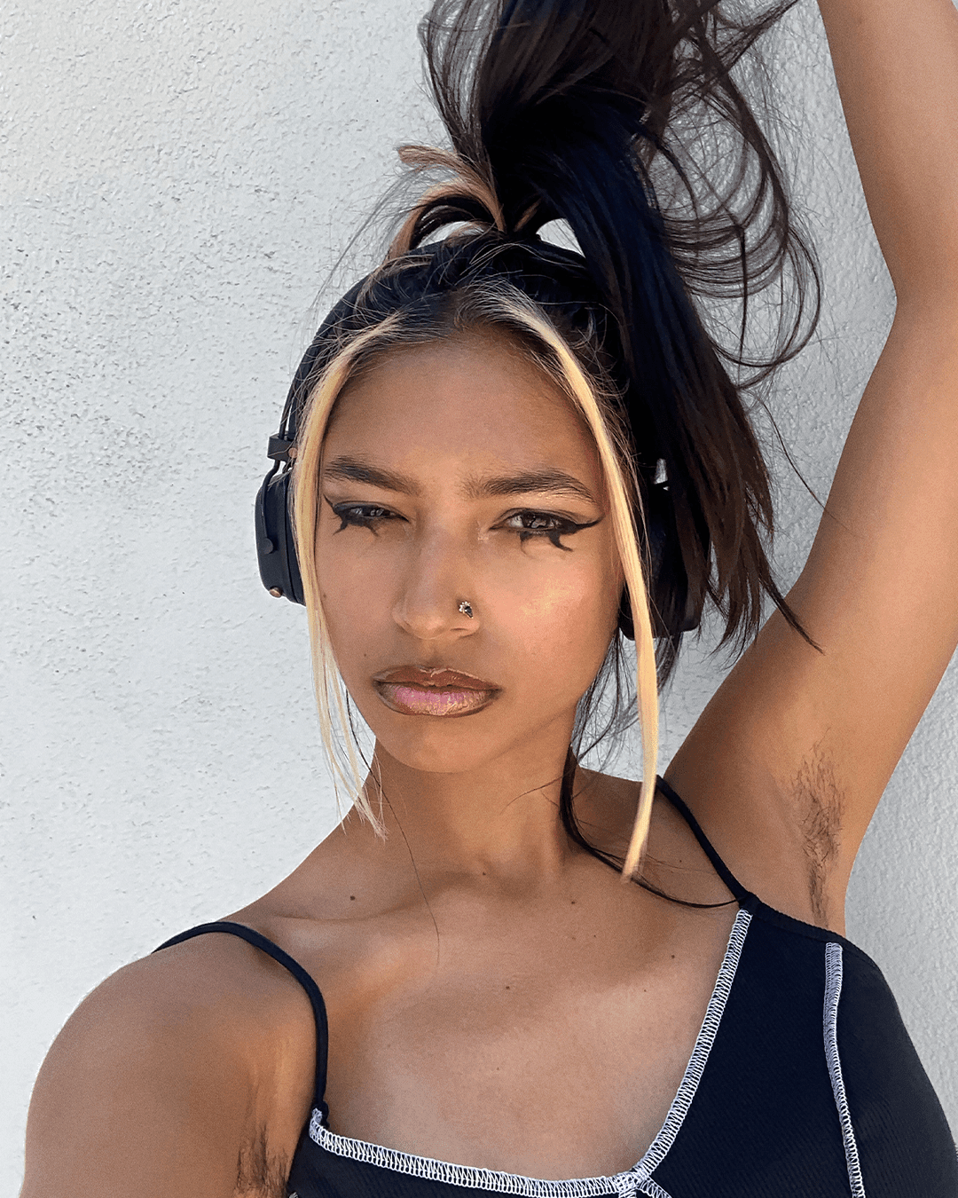 Tara's selfie. They're wearing headphones and confidently holding up their ponytail above their head and looking into camera.