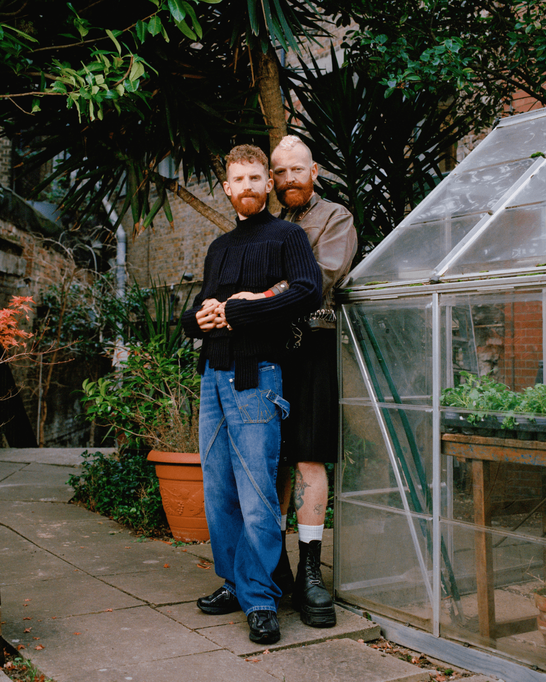 Tom and Shugs stand next to a greenhouse, embracing