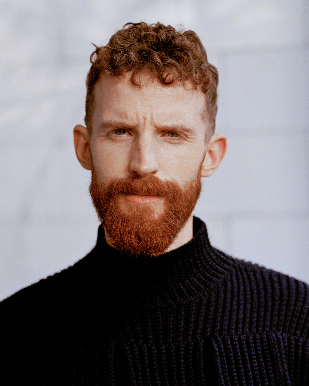 Shugs looks at the camera in front of a white tile backdrop.