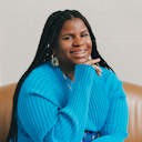 Ericka Hart, wearing a light blue sweater and smiling with her hand rested on her chin.