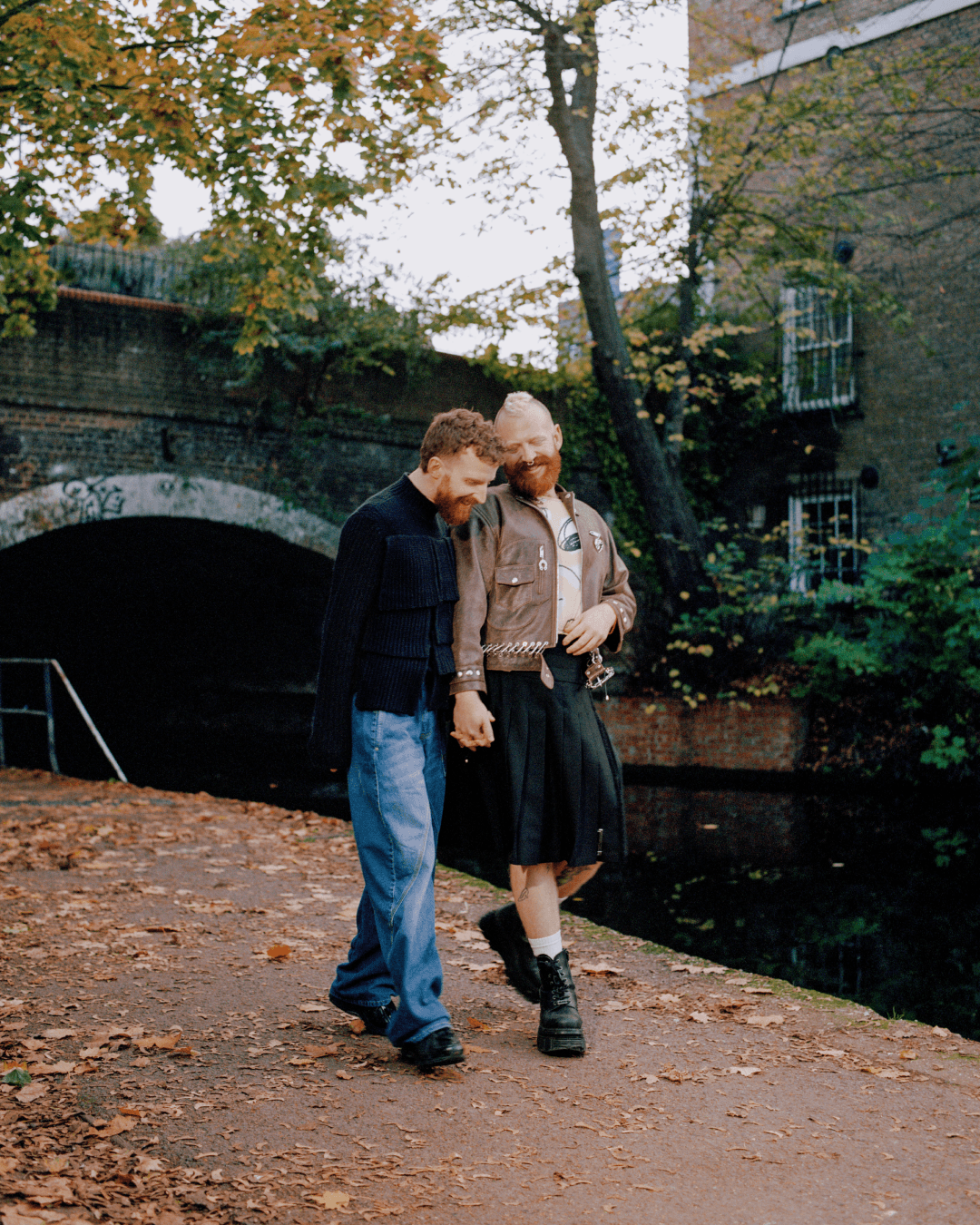 Tom and Shugs walk by a canal, holding hands and laughing.