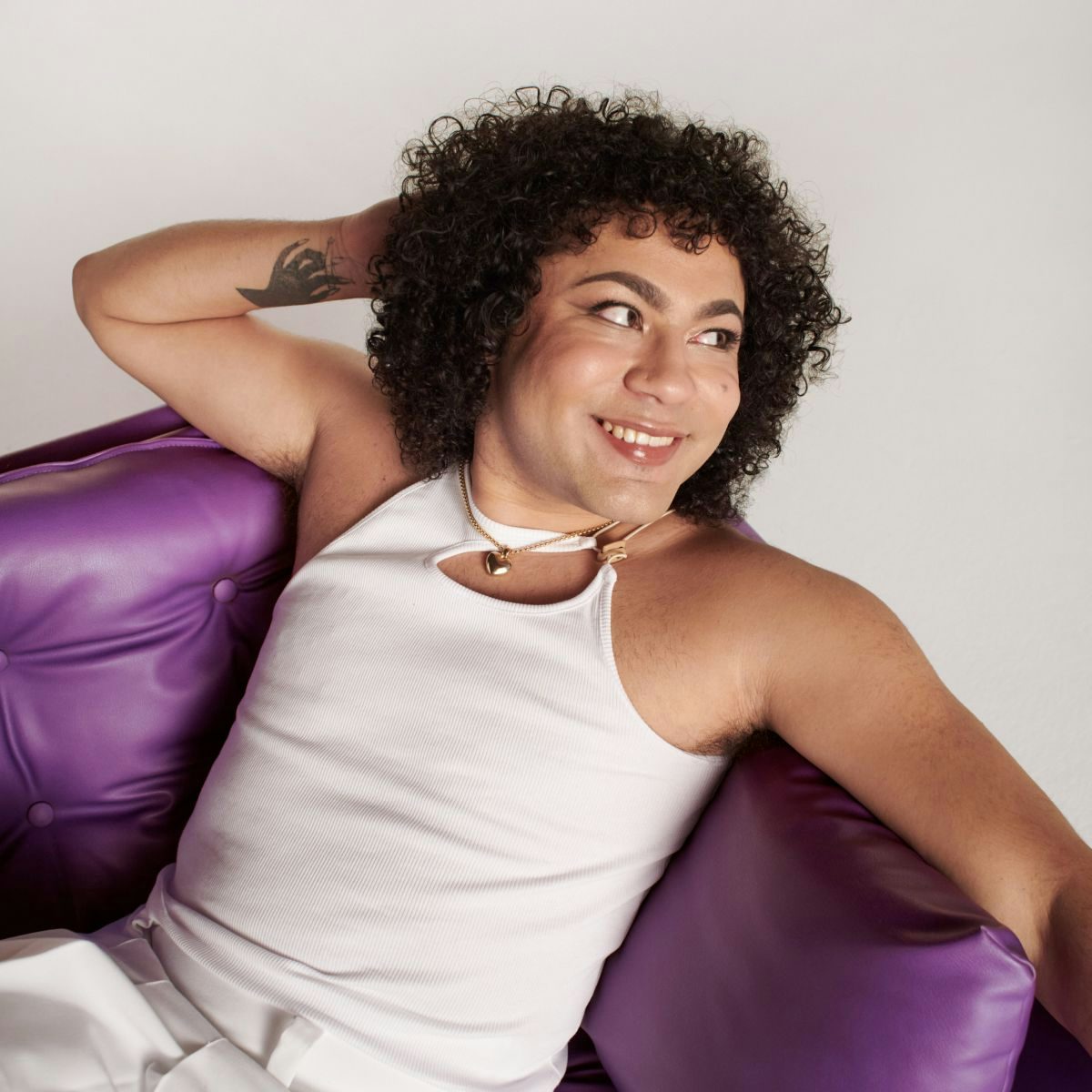 A portrait of Travis looking off-camera, seated on a purple couch
