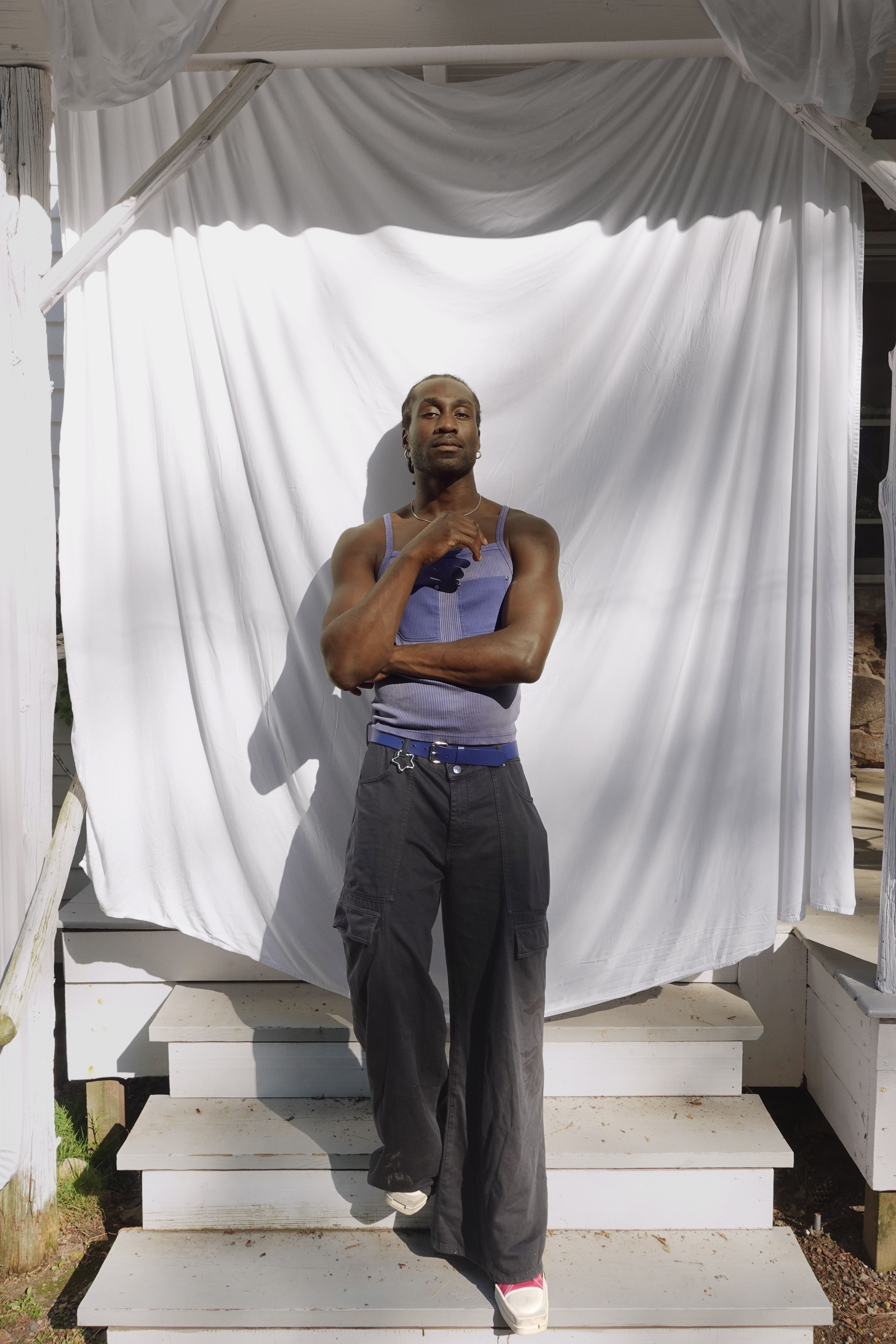 DeVonn Francis standing on gray stairs with a white fabric back drop wearing jeans and a purple tank top