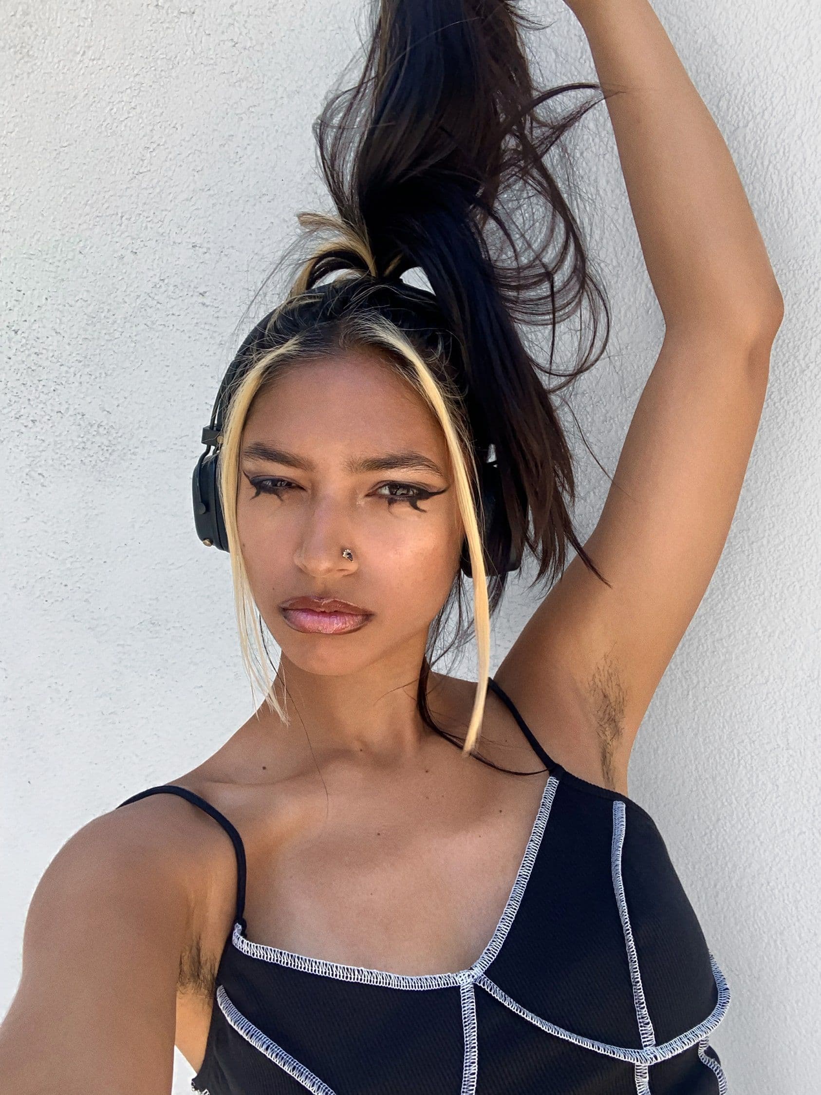 Tara's selfie. They're wearing headphones and confidently holding up their ponytail above their head and looking into camera.