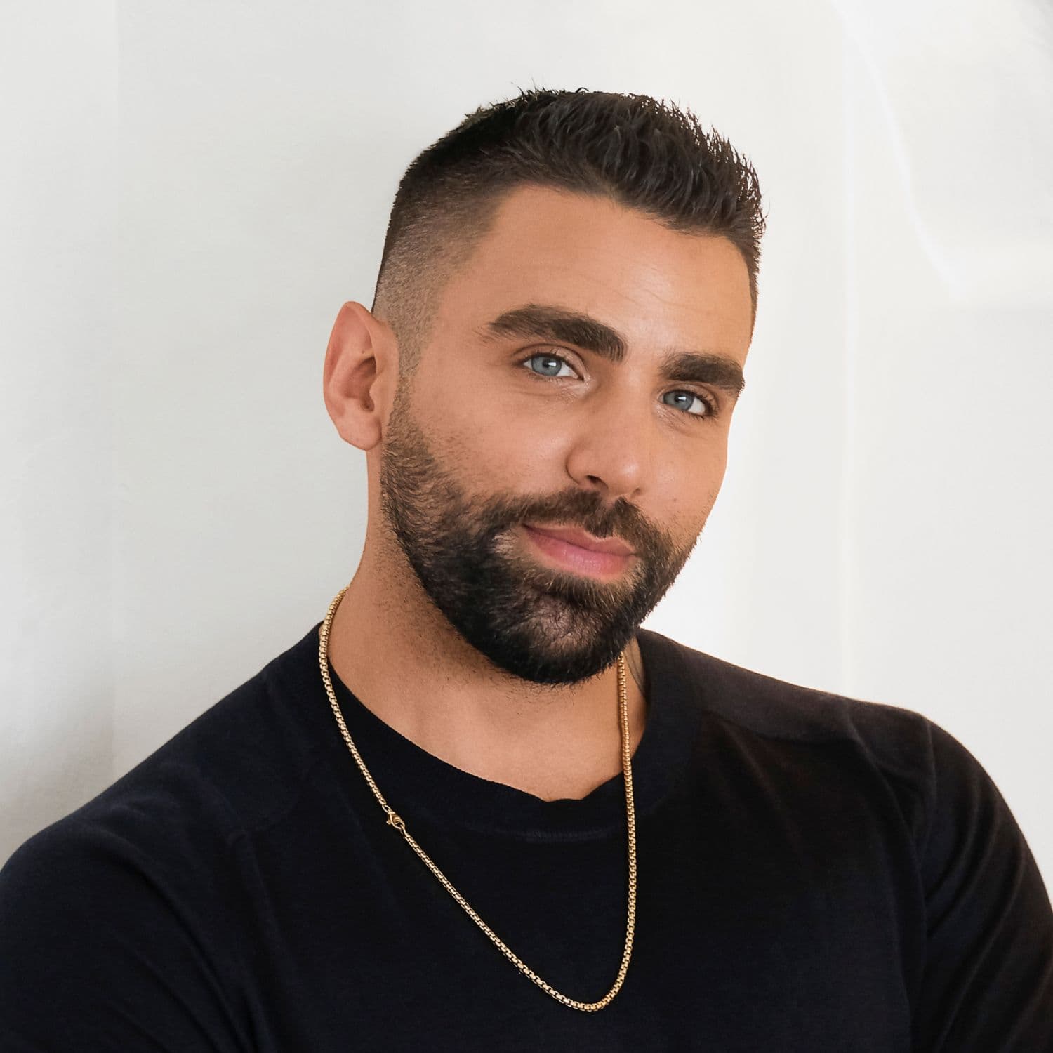 A portrait of Phillip leaning up against a wall. He's smiling with his arms crossed.