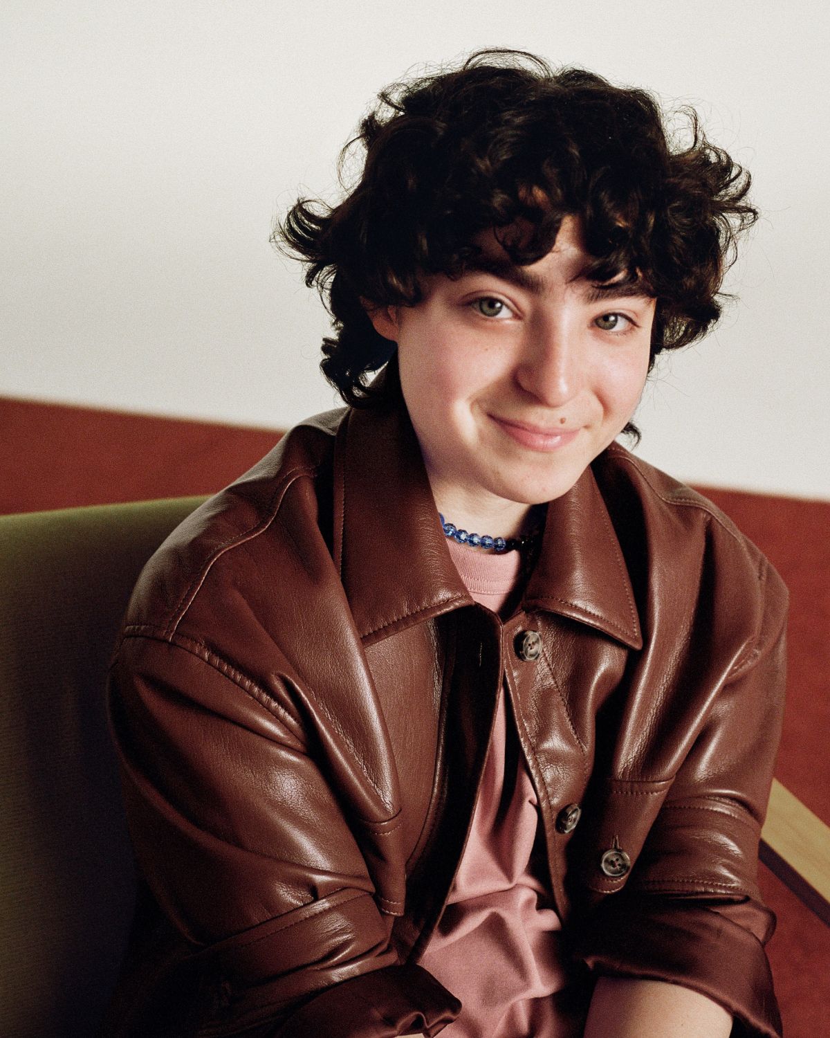 Claud standing in front and looking into the camera with a gentle smile, holding onto the front of a green jacket