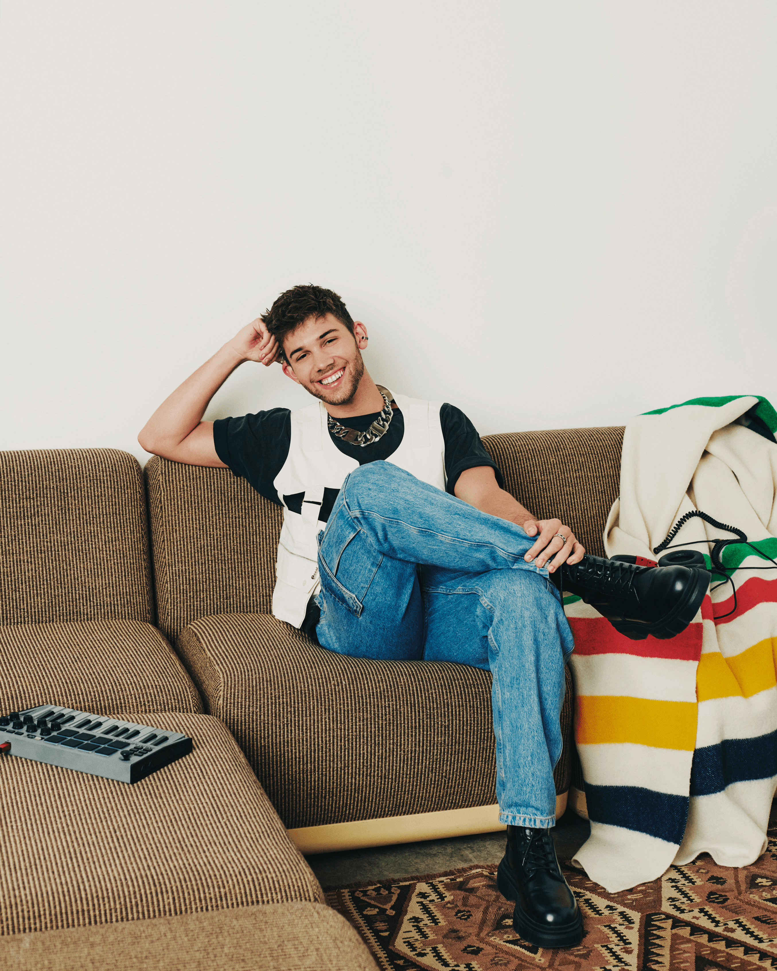 Grant Knoche seating on a tan sofa with his arm propping his head. He's smiling.